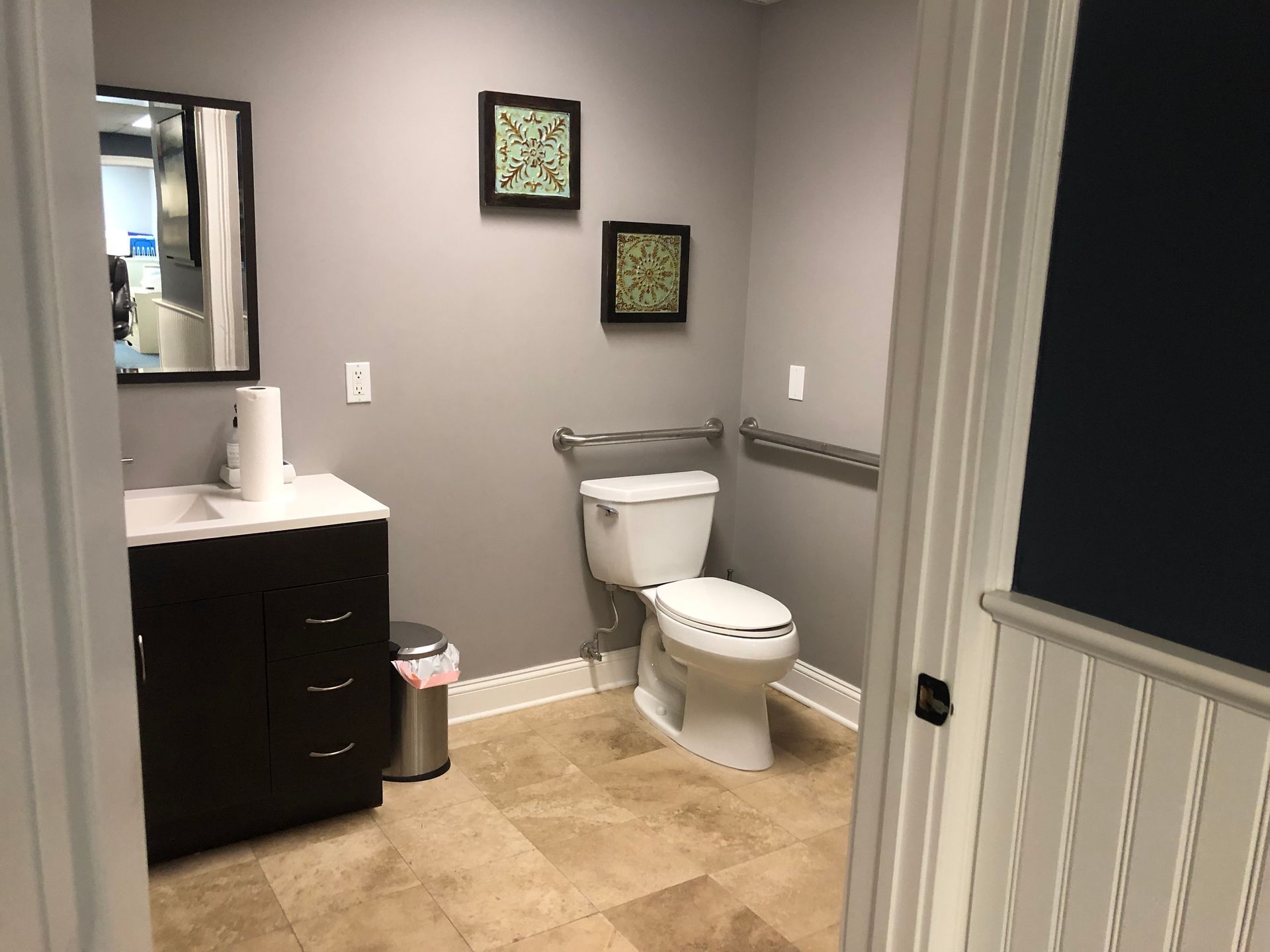 Bathroom with gray walls, beige tile floor, toilet, vanity, and safety bar.