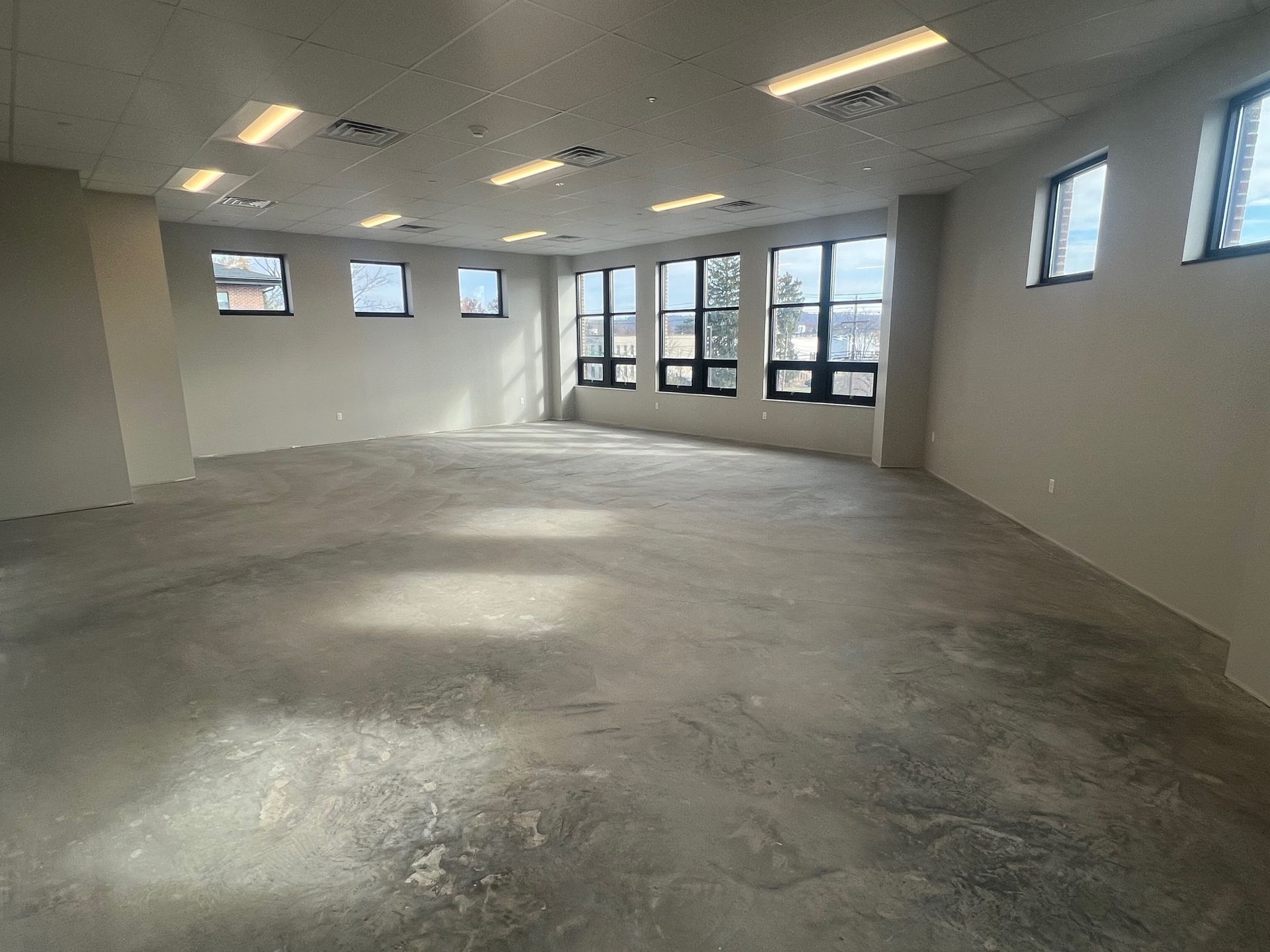 Empty room with gray concrete floor, white walls, and multiple windows.