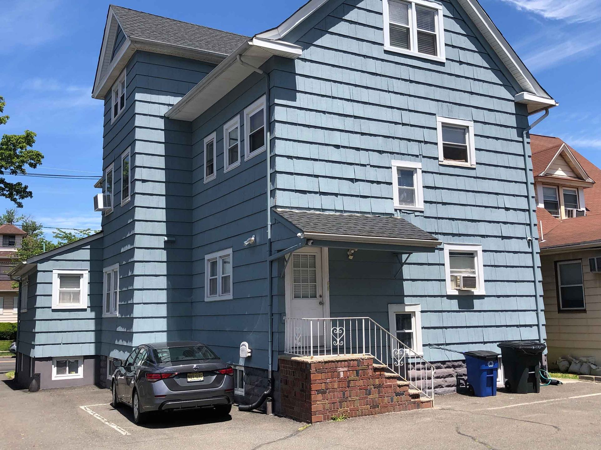 Blue two-story house with a parked black car in front and a small brick stoop.