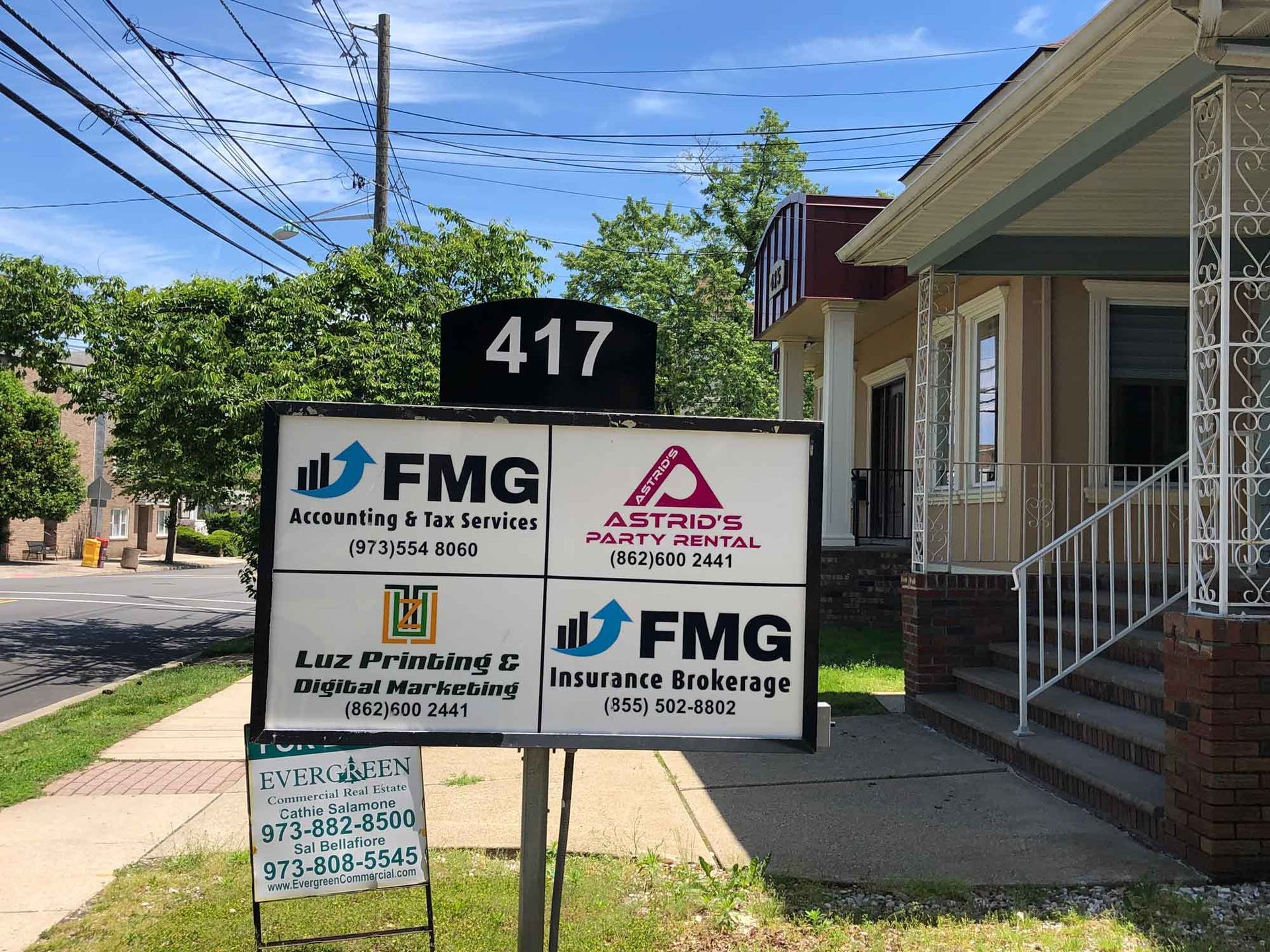 Sign outside 417 with FMG and other business signs beside a house on a sunny street
