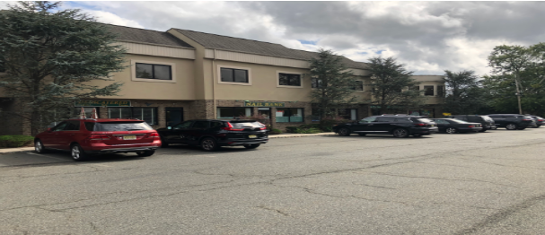 A two-story, tan-colored commercial building with parked cars in front under a partly cloudy sky.