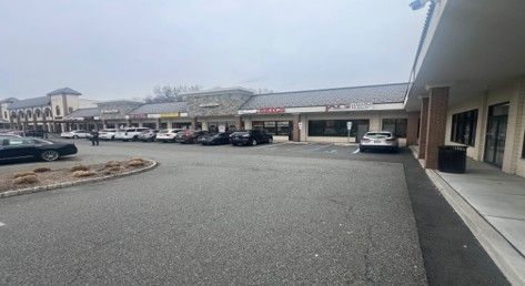 A paved parking lot in front of a long, single-story commercial strip mall under an overcast sky.