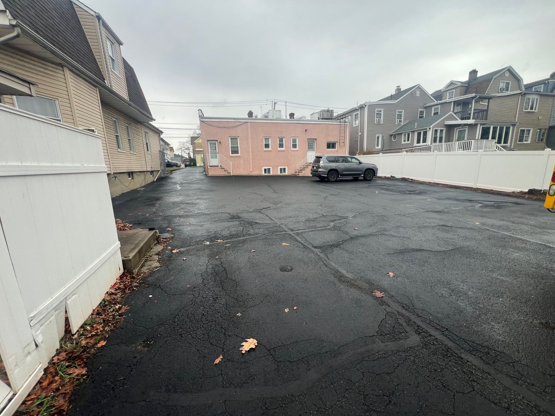 An asphalt parking lot sits between residential buildings, with a gray SUV parked near a pink single-story structure.