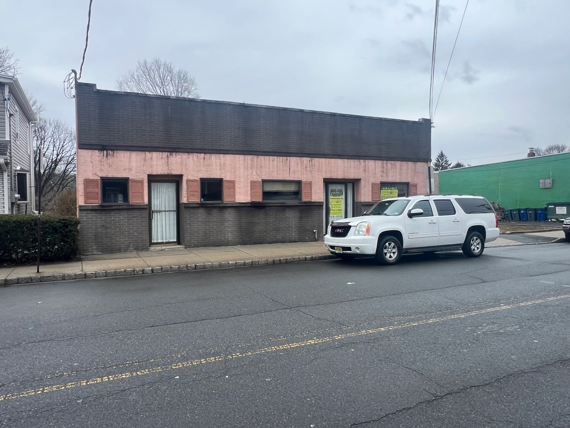 A single-story, pink commercial building with a dark facade and a white SUV parked out front on a grey, paved street.