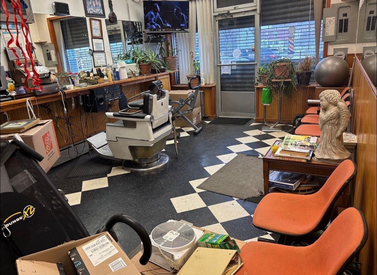 Cluttered workshop with tools, shelves, chairs, and a checkered floor near a glass door and window.