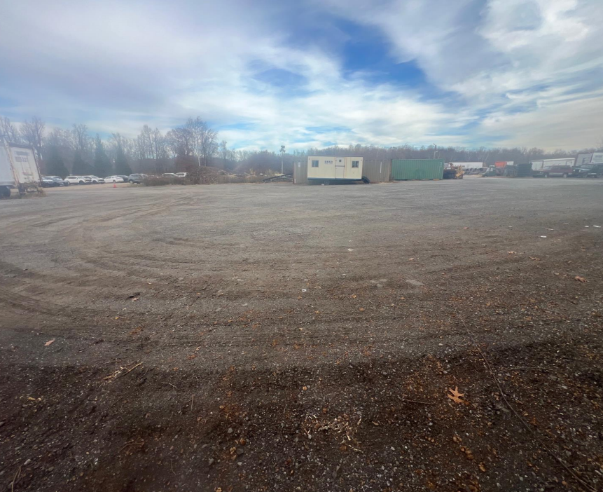 Gravel parking lot under a cloudy sky. A white trailer sits near trees in the distance.