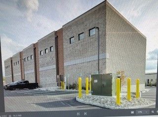 Large brick building with a few windows, black truck parked in front; electrical box with yellow bollards.