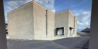 A large, rectangular concrete building with a loading dock and a dark roof.