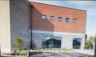 Brick and stone building with windows, some at ground level. Parking lot in front.