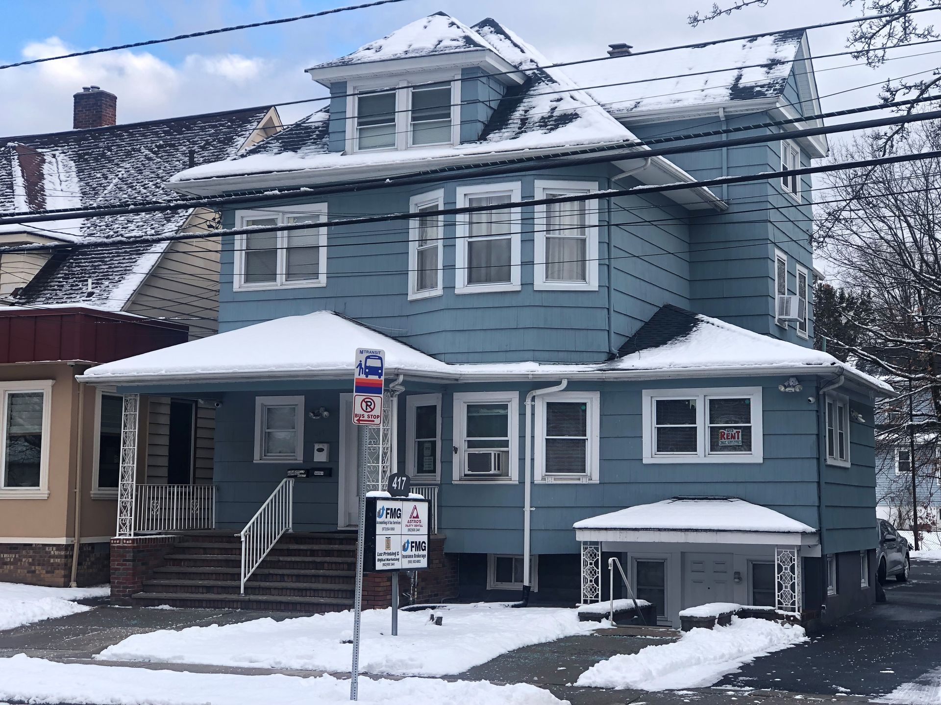 Blue multi-story house covered in snow with a front porch and small driveway.
