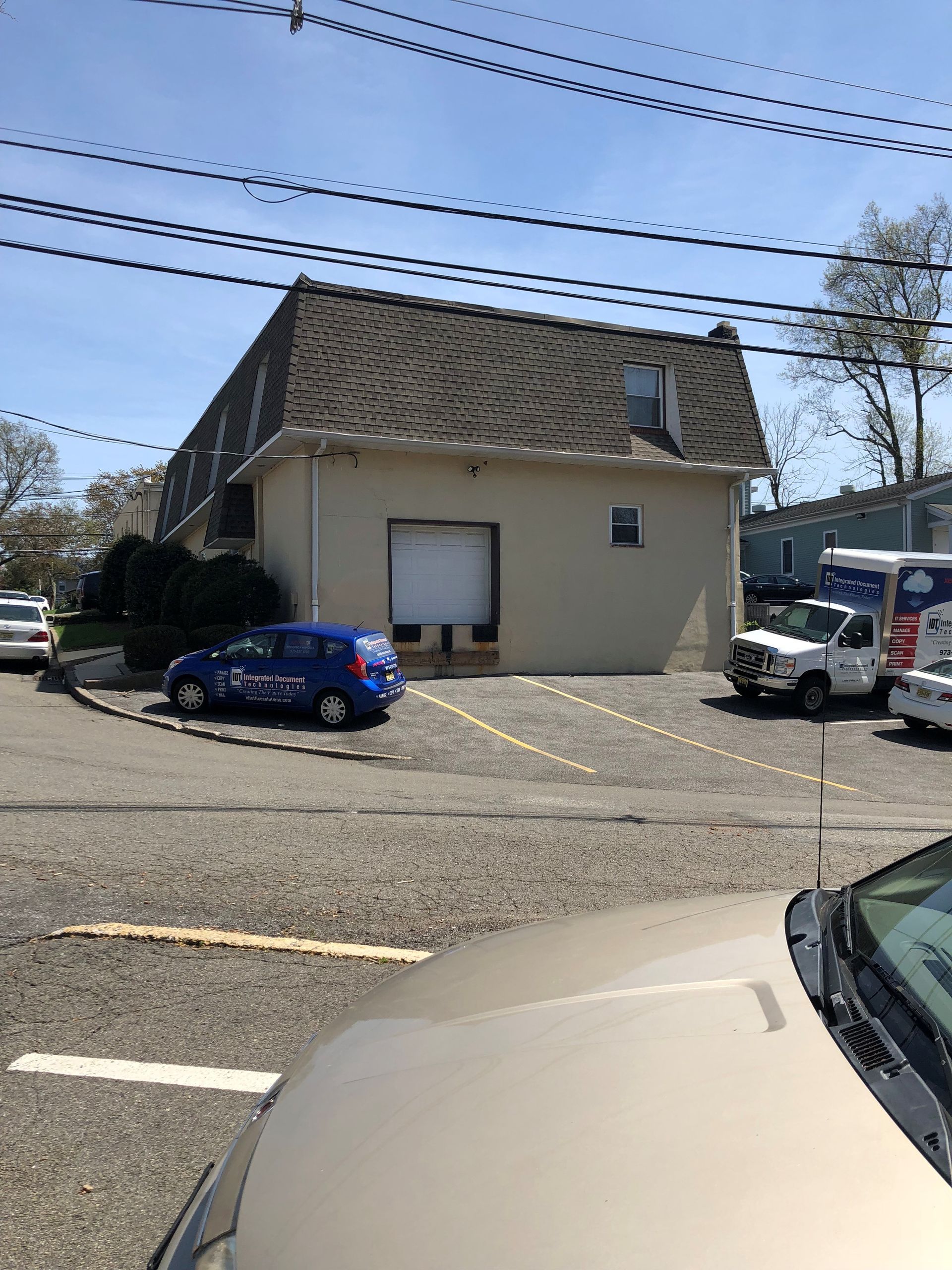 Beige building with a roll-up door, parked cars, and overhead power lines.