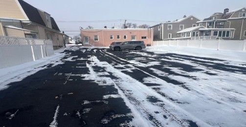 Snowy parking lot with car tracks, SUV parked near pink building and houses.