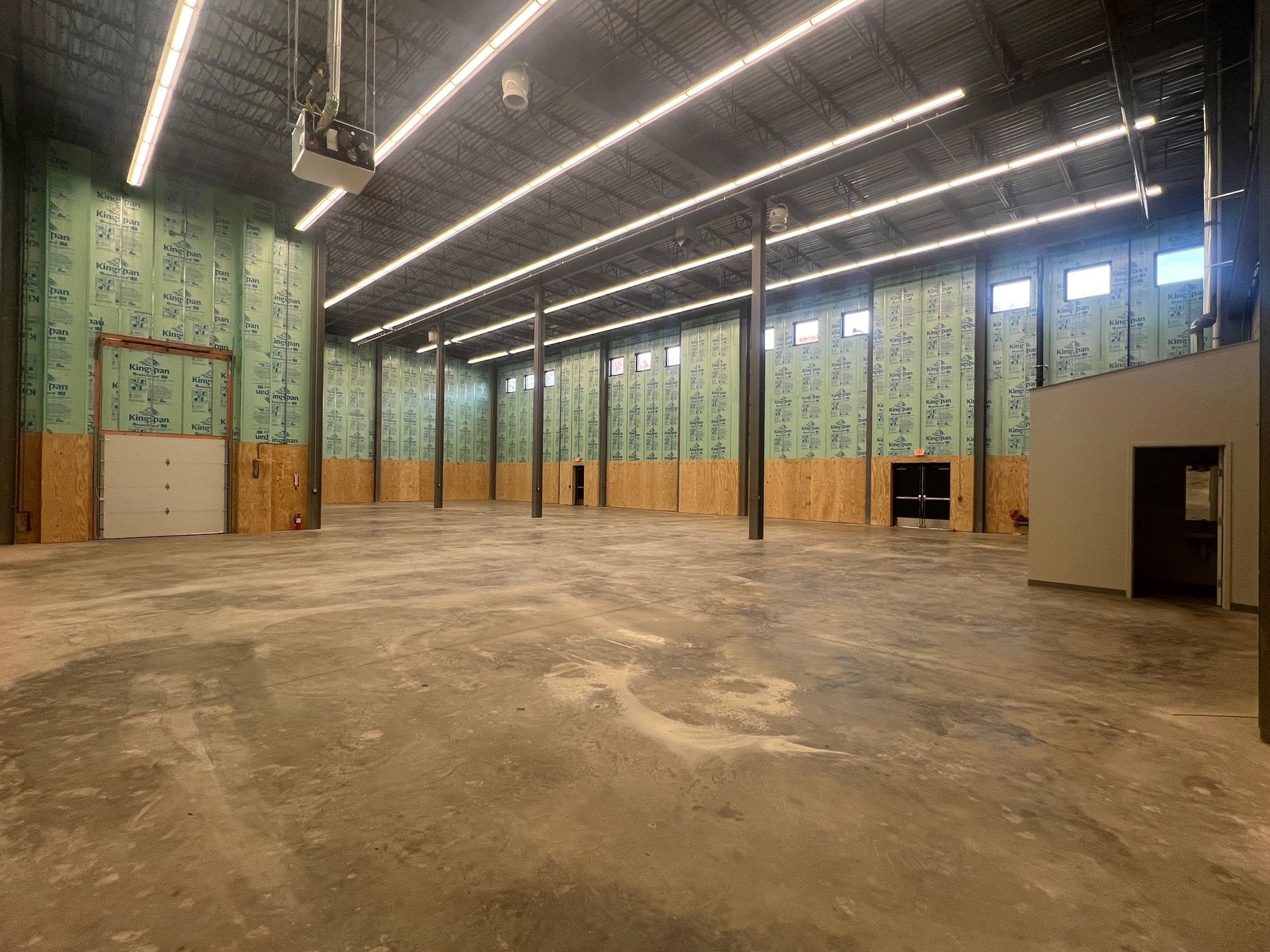 Interior of an unfinished industrial building with concrete floor, metal beams, and overhead lighting.