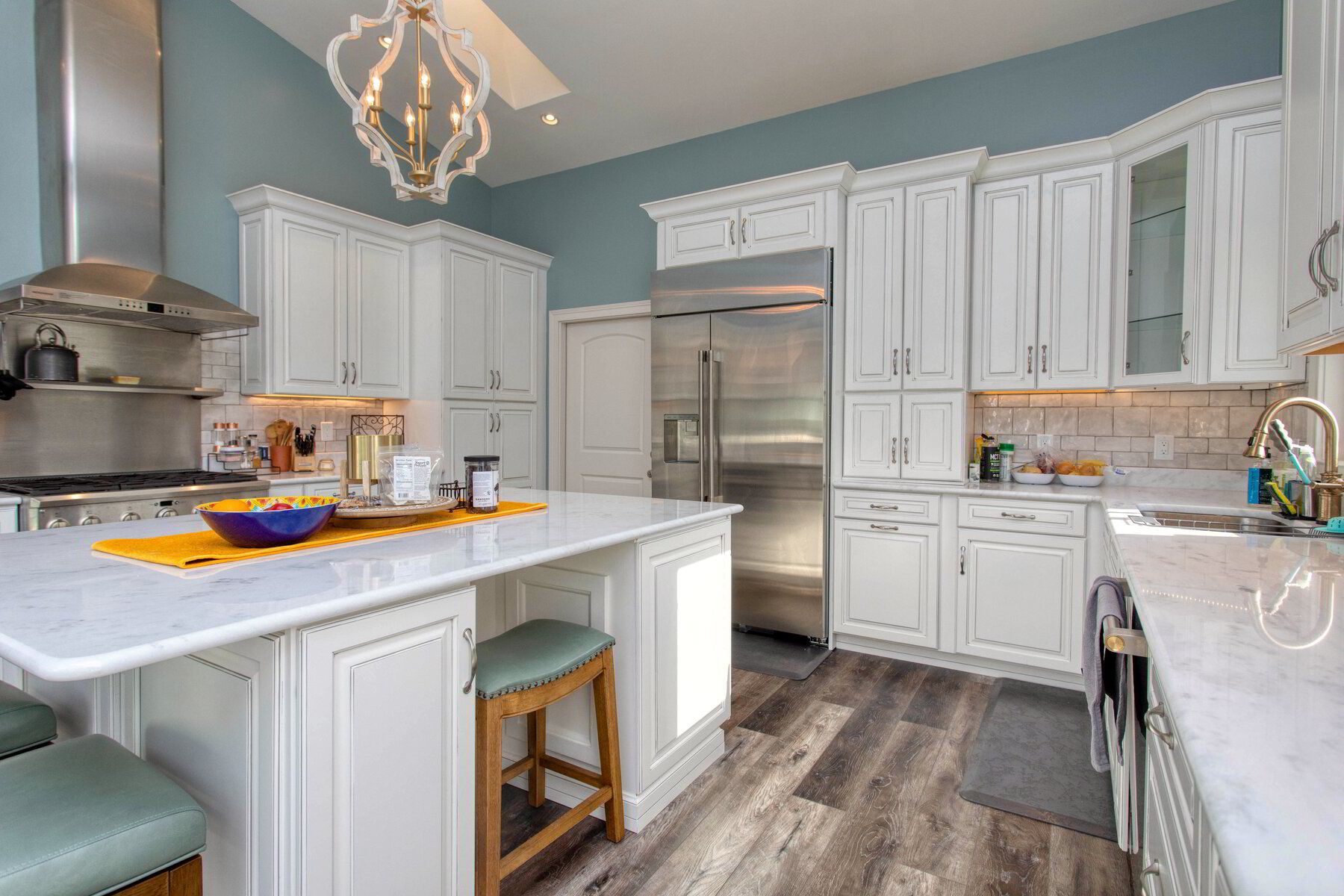 A kitchen with white cabinets , stainless steel appliances , and a large island.