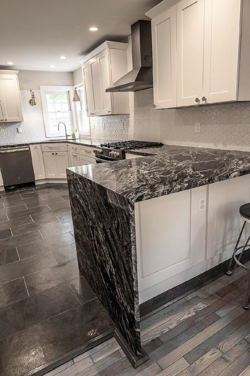 A kitchen with a black granite counter top and white cabinets.