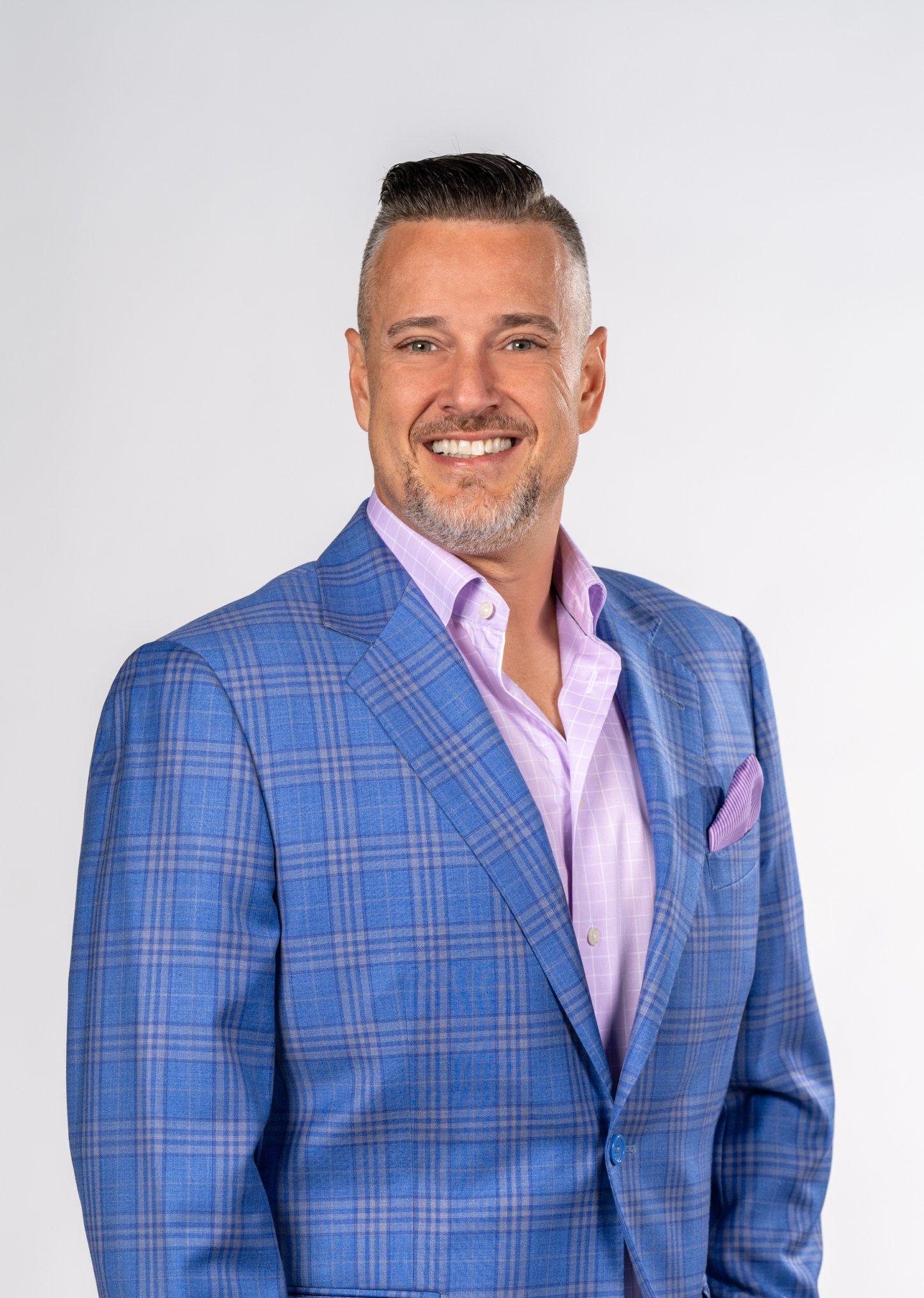 A man in a blue suit and pink shirt is smiling for the camera.