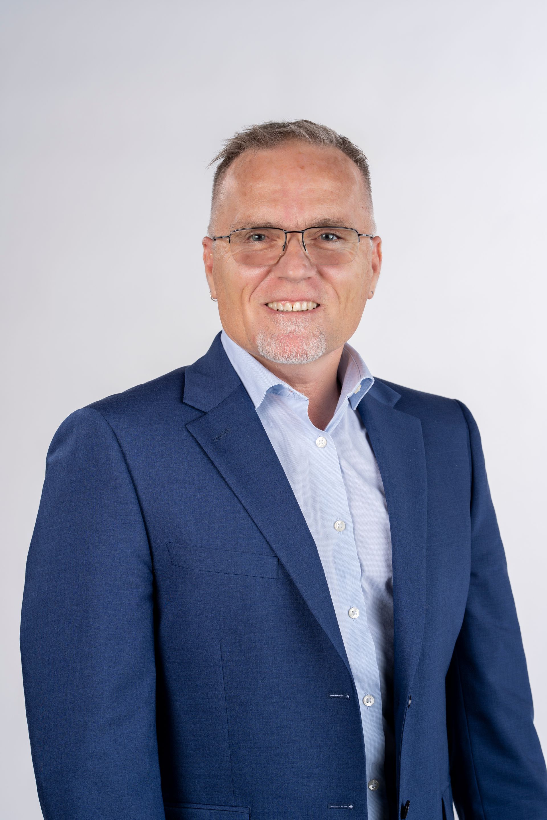 A man in a blue suit and glasses is smiling for the camera.