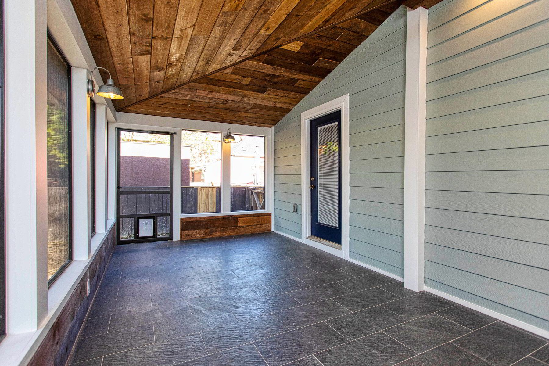 An empty porch with a wooden ceiling and a screen door.