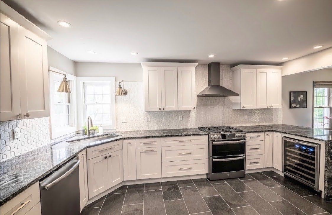 A kitchen with white cabinets , black counter tops , a stove and a refrigerator.