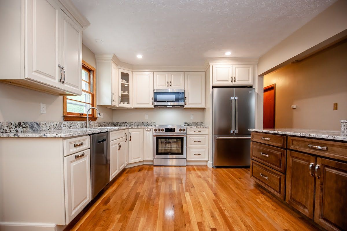 A kitchen with hardwood floors , white cabinets , stainless steel appliances and a refrigerator.
