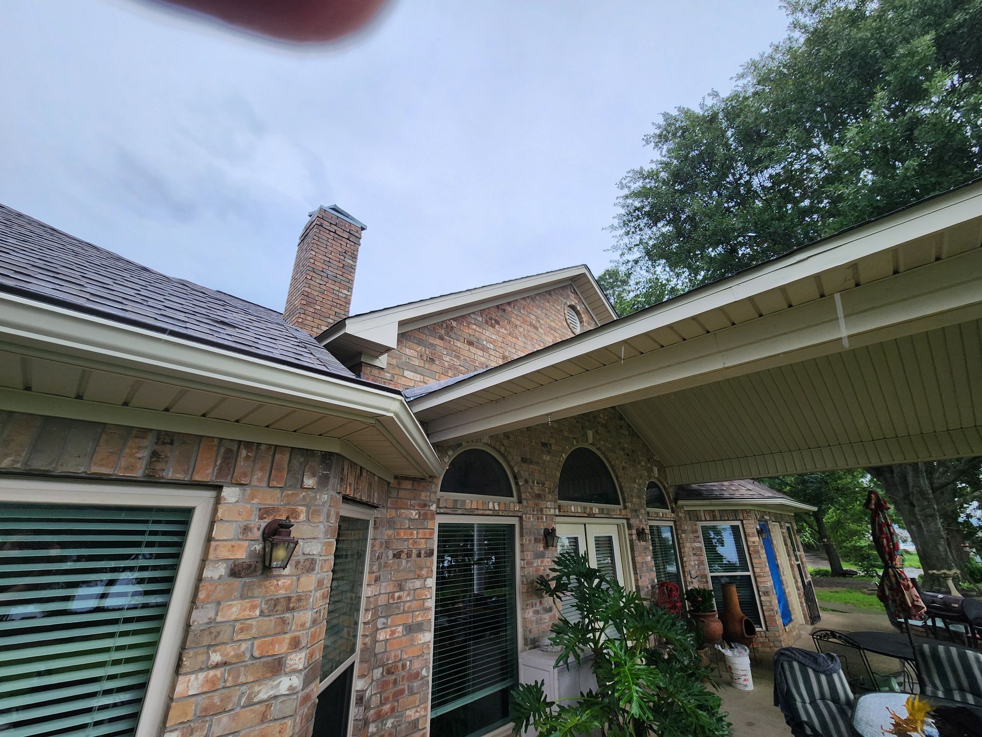 A brick house with a covered patio and a chimney on the roof.