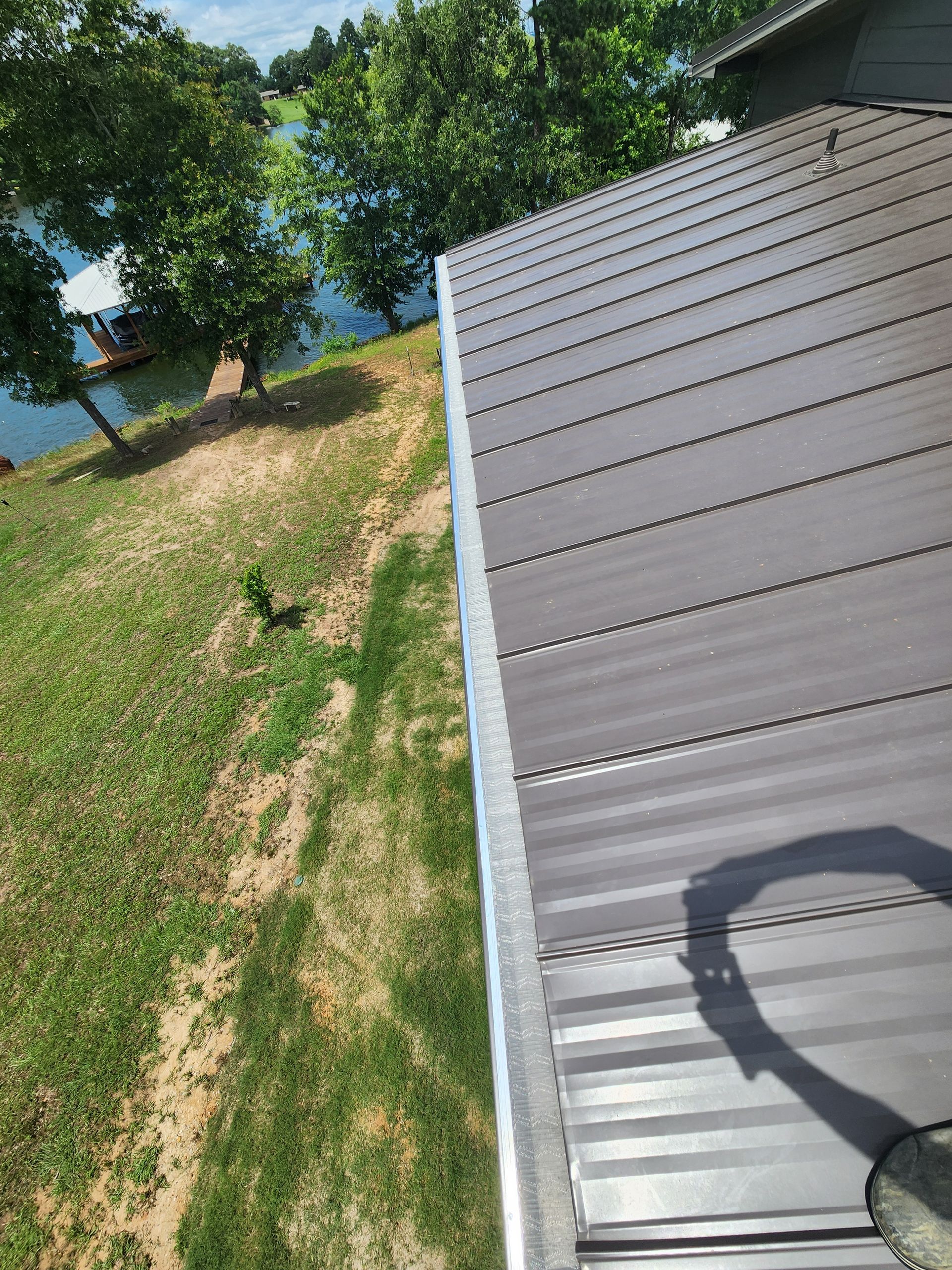 A roof with a gutter on it is sitting on top of a grassy hill next to a body of water.
