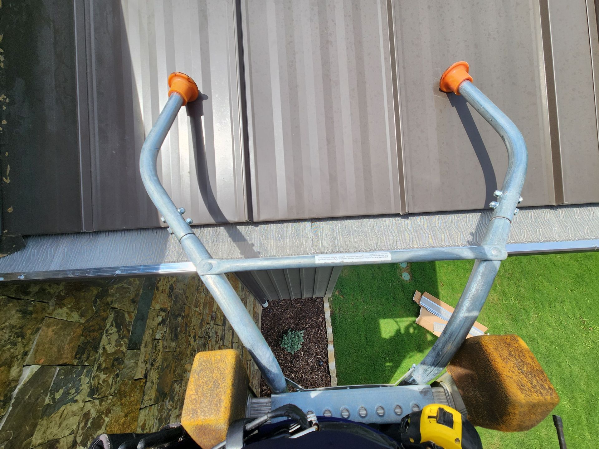 A person is standing on a ladder looking down at a roof.