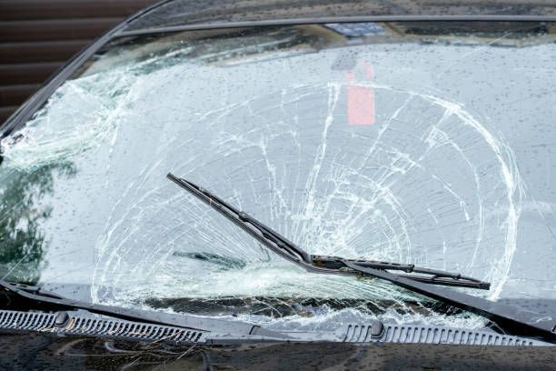 Shattered windshield of a car; wiper blades in place; visible cracks radiating from impact point.
