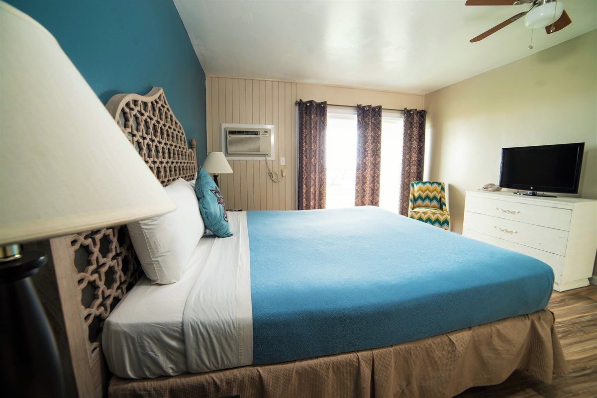 A king-size bed with turquoise bedding in a motel room, with a TV and blue accent wall.