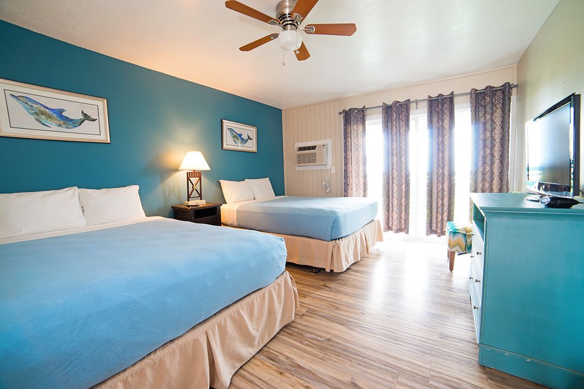 Hotel room with two beds, turquoise walls, balcony, and a TV.