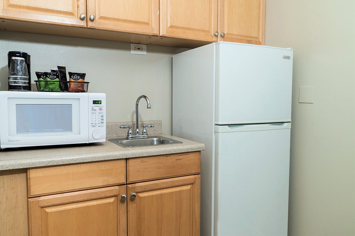 Small kitchenette with microwave, sink, fridge, and cabinets.