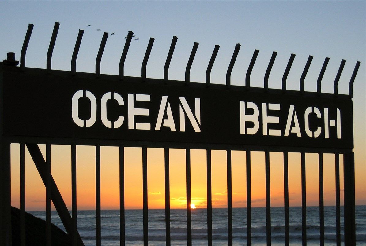 Sunset through a gate at Ocean Beach, California. The sky is orange and the ocean is dark.