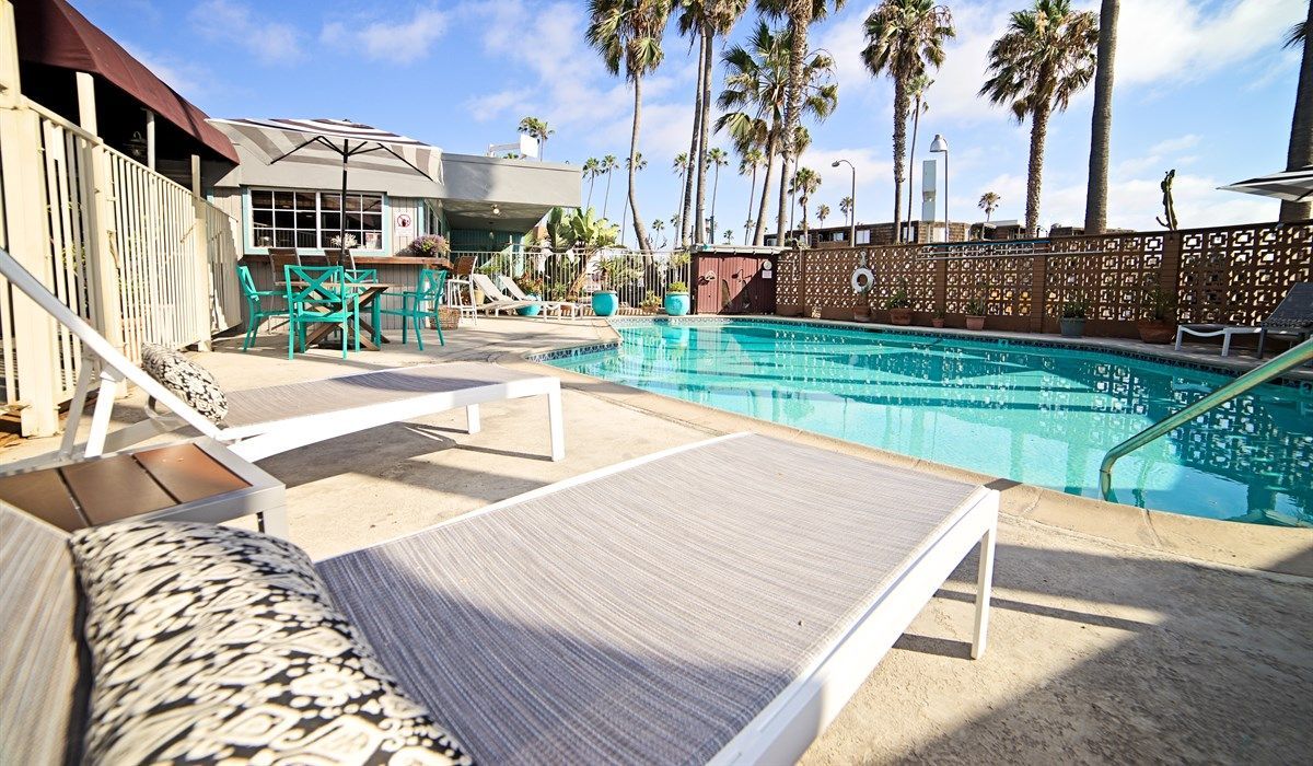 Poolside scene with lounge chairs, turquoise chairs, and palm trees under a bright blue sky.