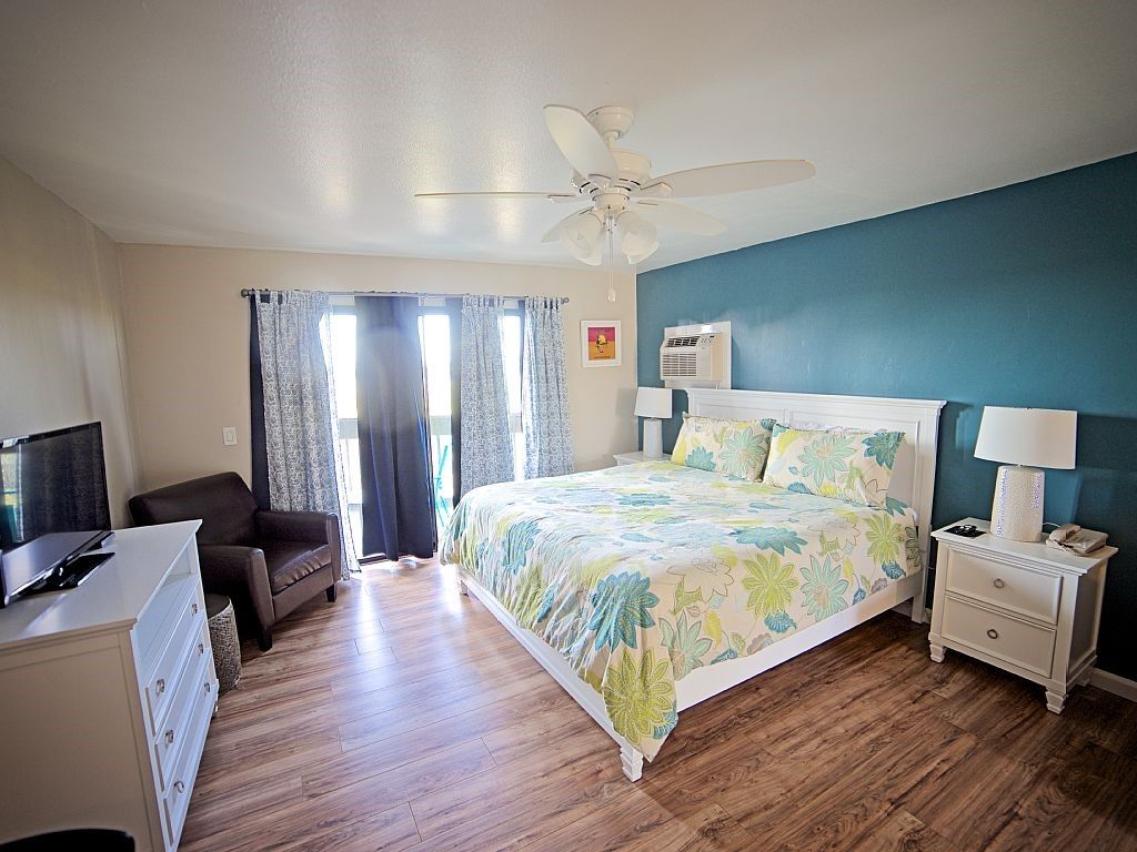 Bedroom with a bed, nightstand, dresser, chair, and balcony doors. Blue accent wall and floral bedding.