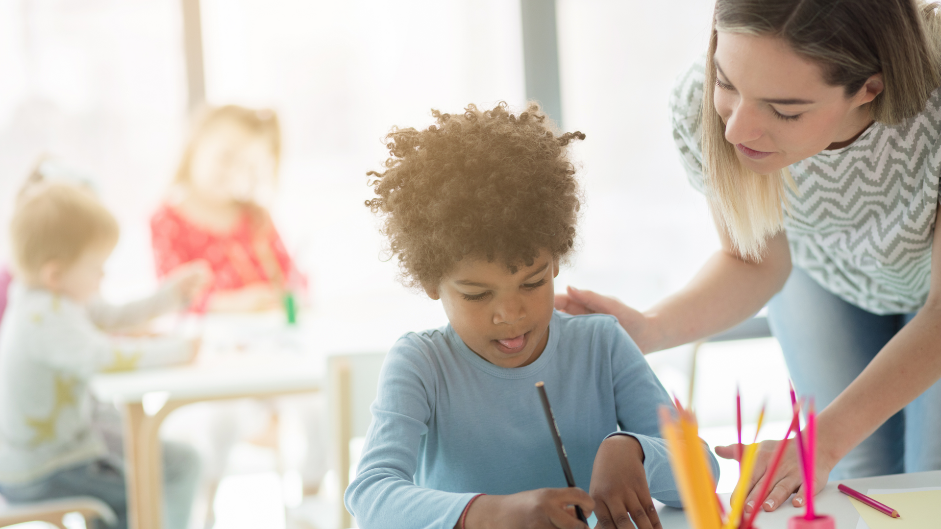 A woman is helping a young boy with his homework in a classroom.