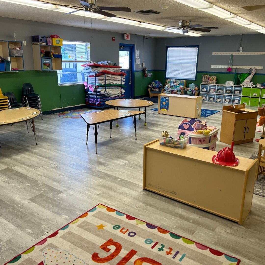 A classroom with tables and chairs and a rug that says little one.