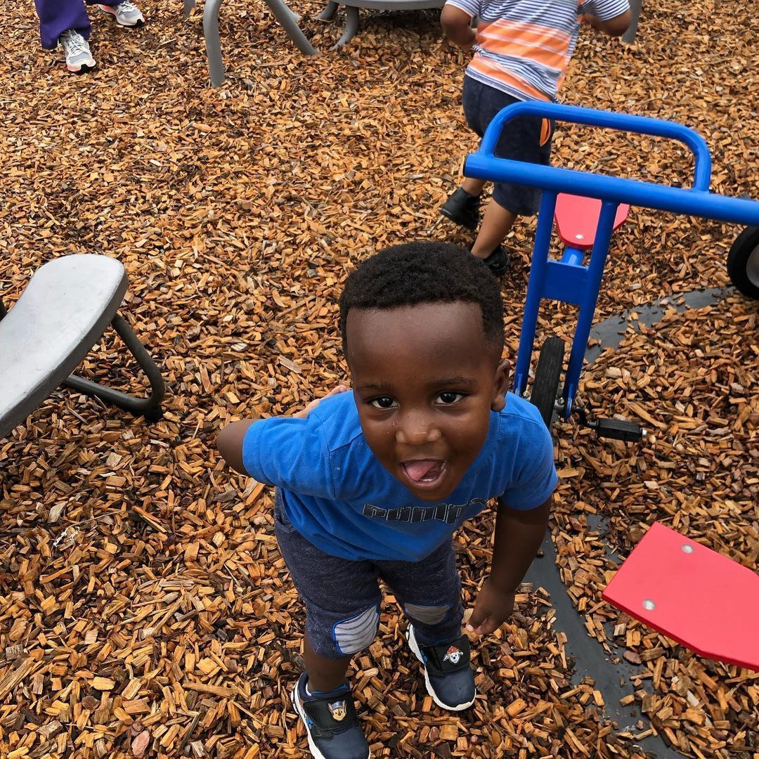 A young boy in a blue shirt is sticking out his tongue at a playground