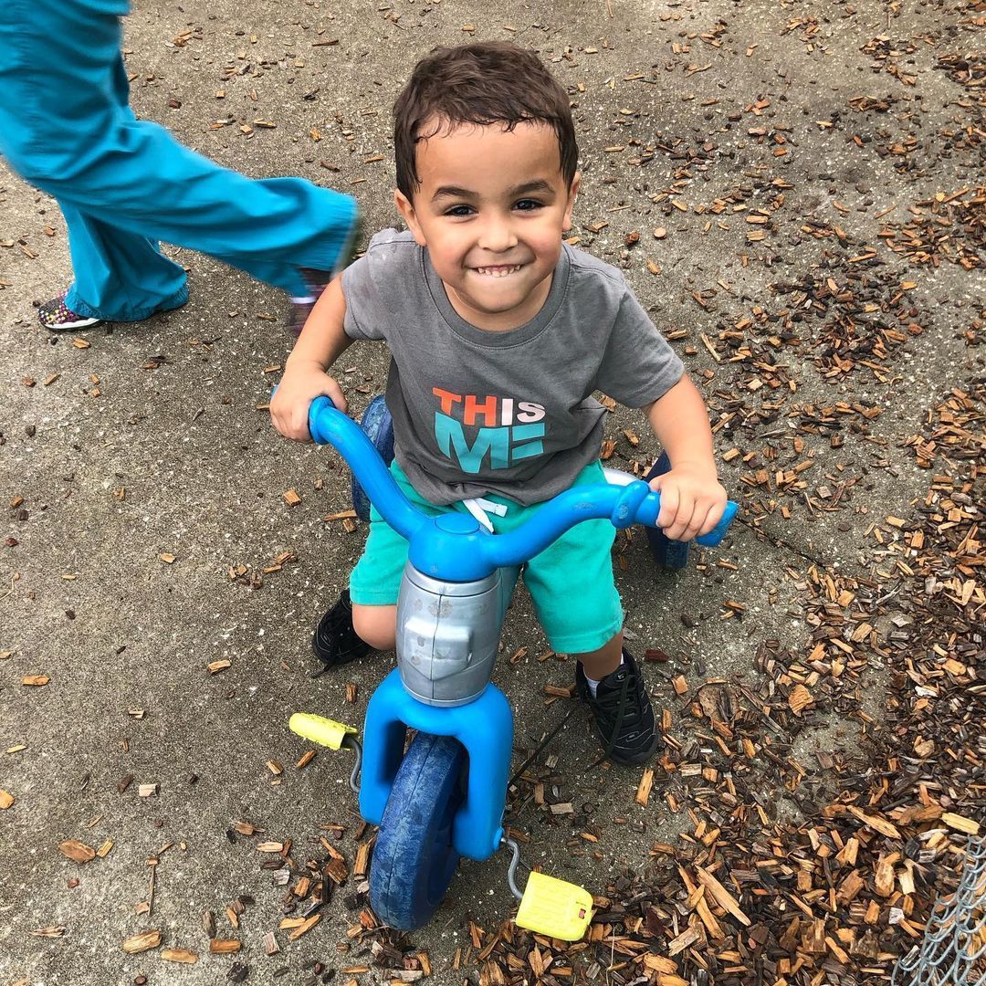 A little boy wearing a shirt that says this me is riding a blue bike