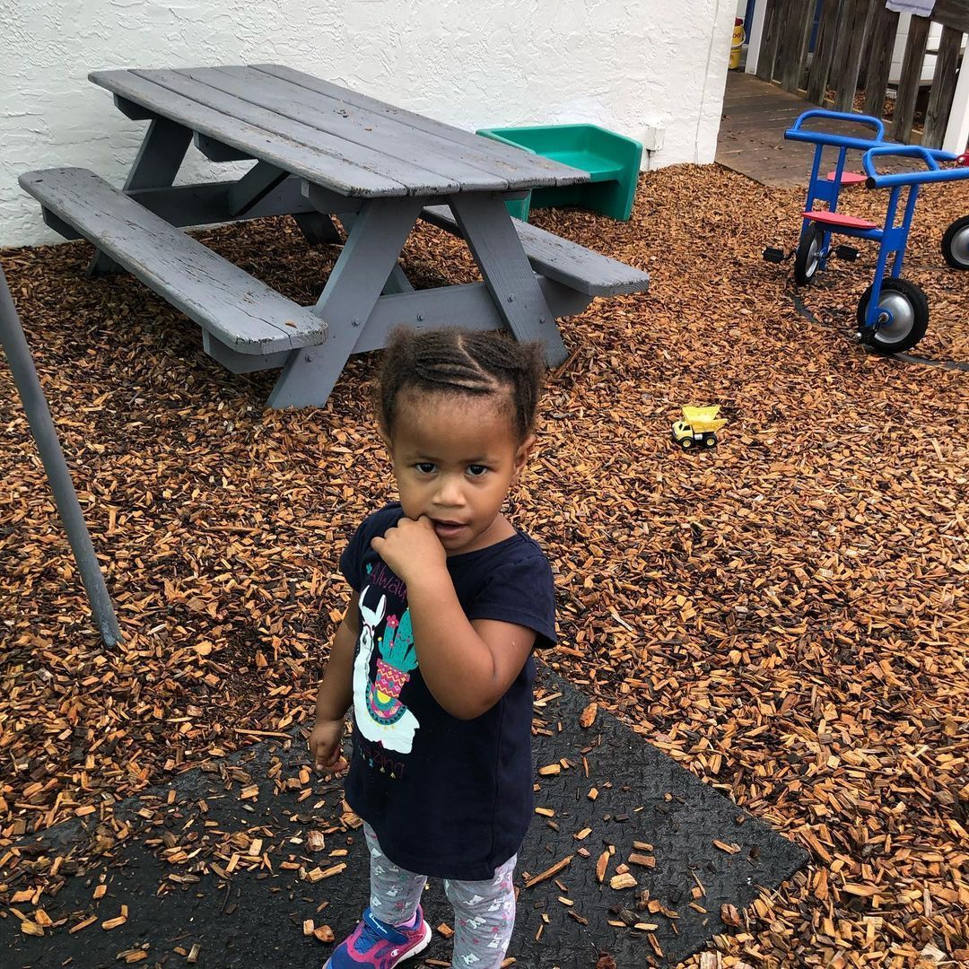 A little girl is standing in front of a picnic table.