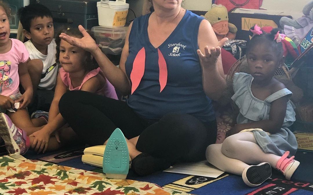 A woman is sitting on the floor with a group of children.