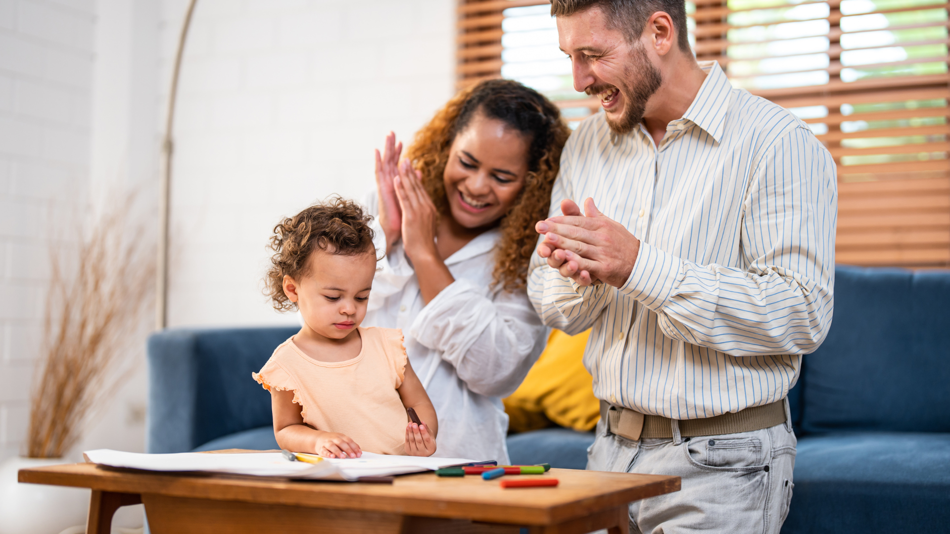 A man and woman are clapping while a little girl sits at a table.