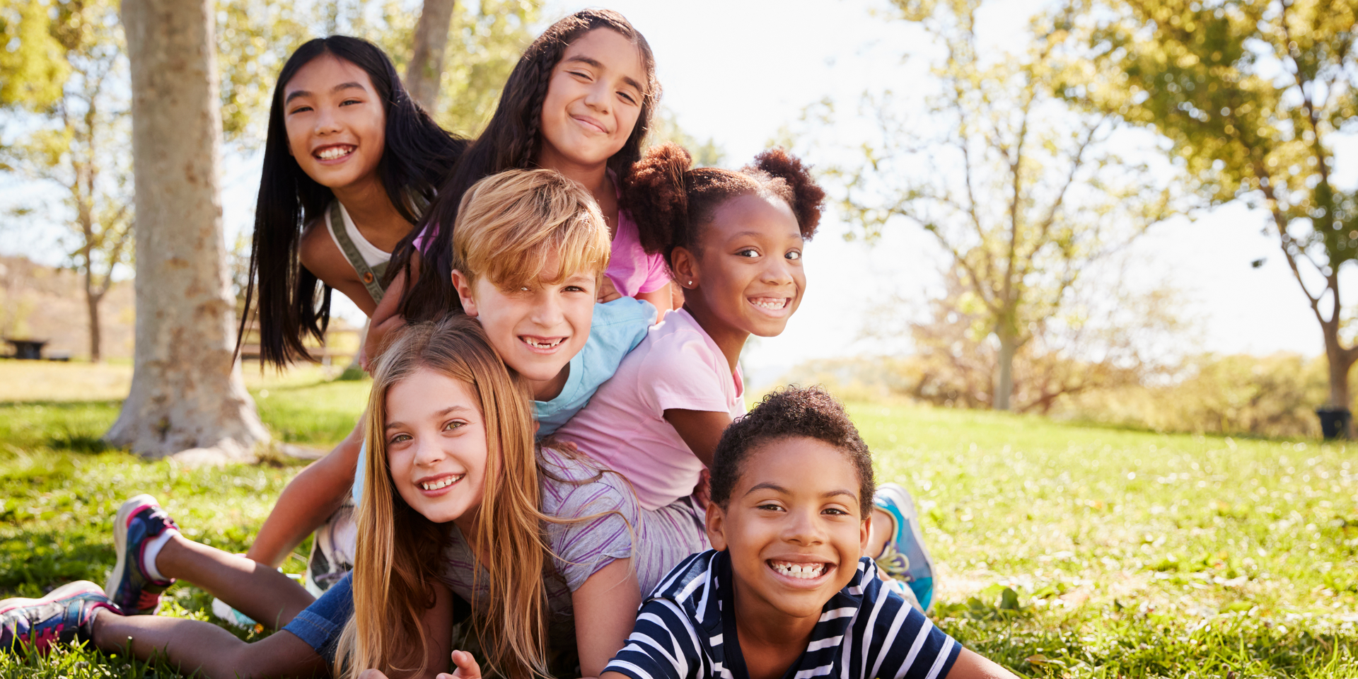 A group of children are laying on top of each other in a park.