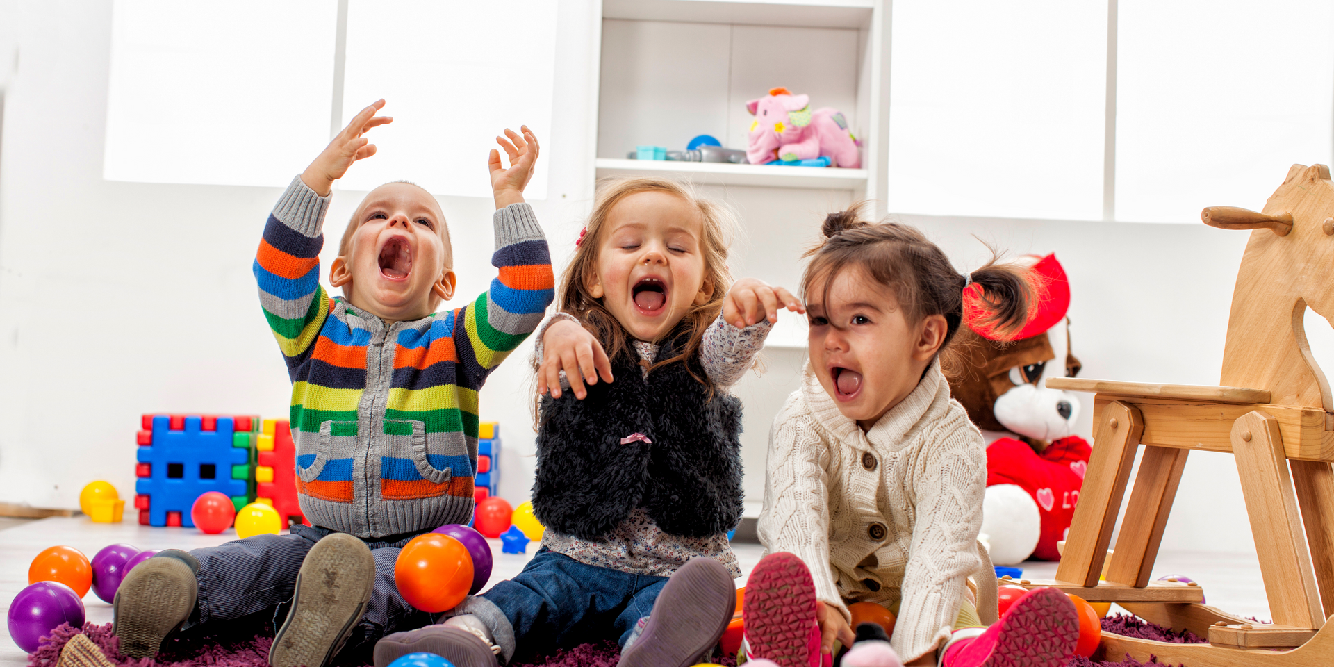 Three children are sitting on the floor playing with toys.