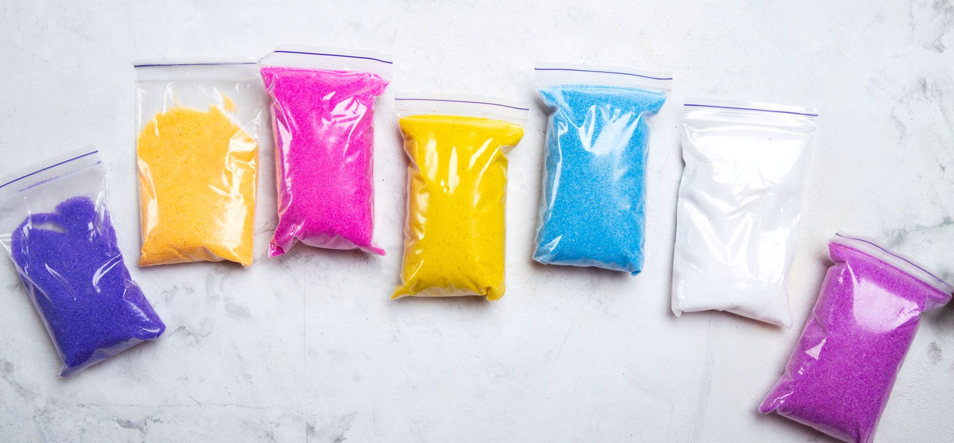 Colorful granular materials in clear plastic zip bags on a white surface.
