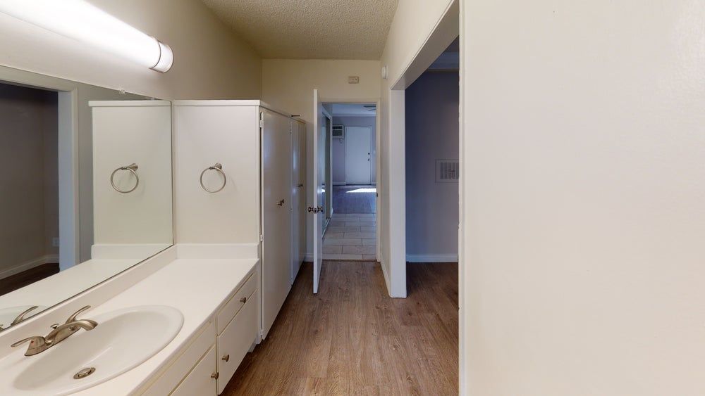 Bathroom with white vanity, cabinets, and a doorway leading to a hallway.