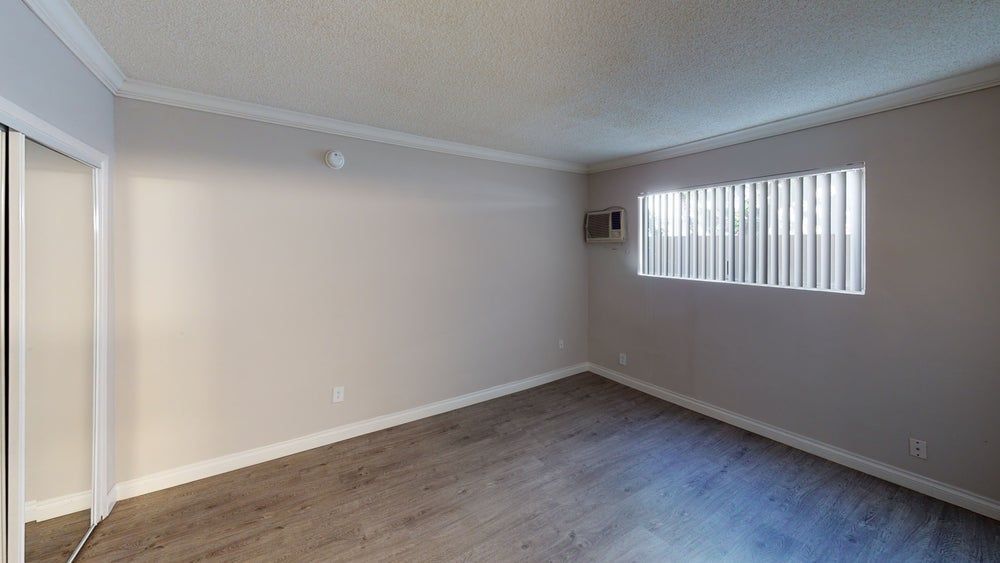 Empty room with light gray walls, window with blinds, and wood-look flooring.