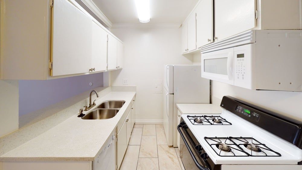 White galley kitchen with cabinets, appliances, and sink.