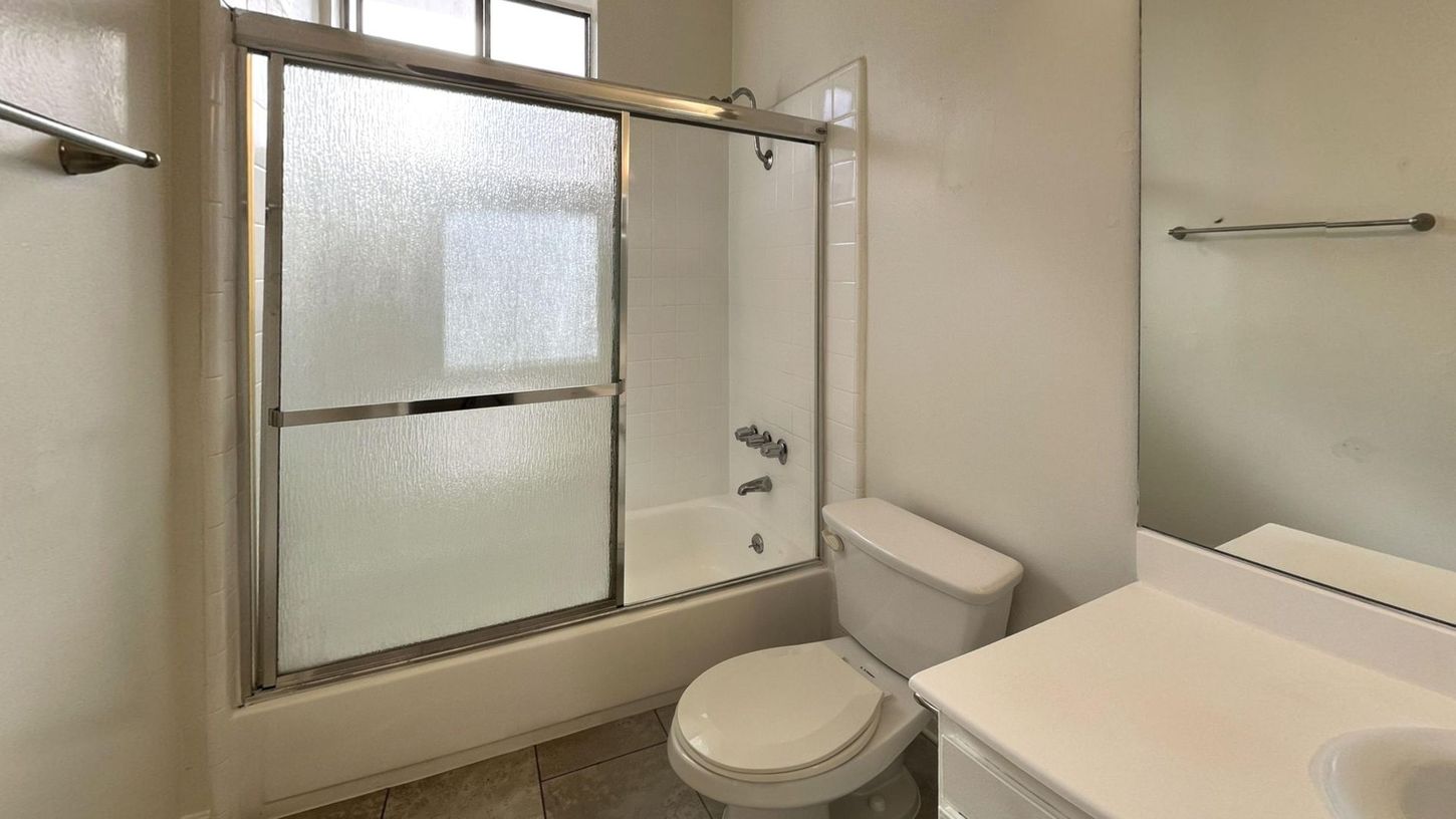 Bathroom with sliding glass shower door, toilet, sink, and towel racks.