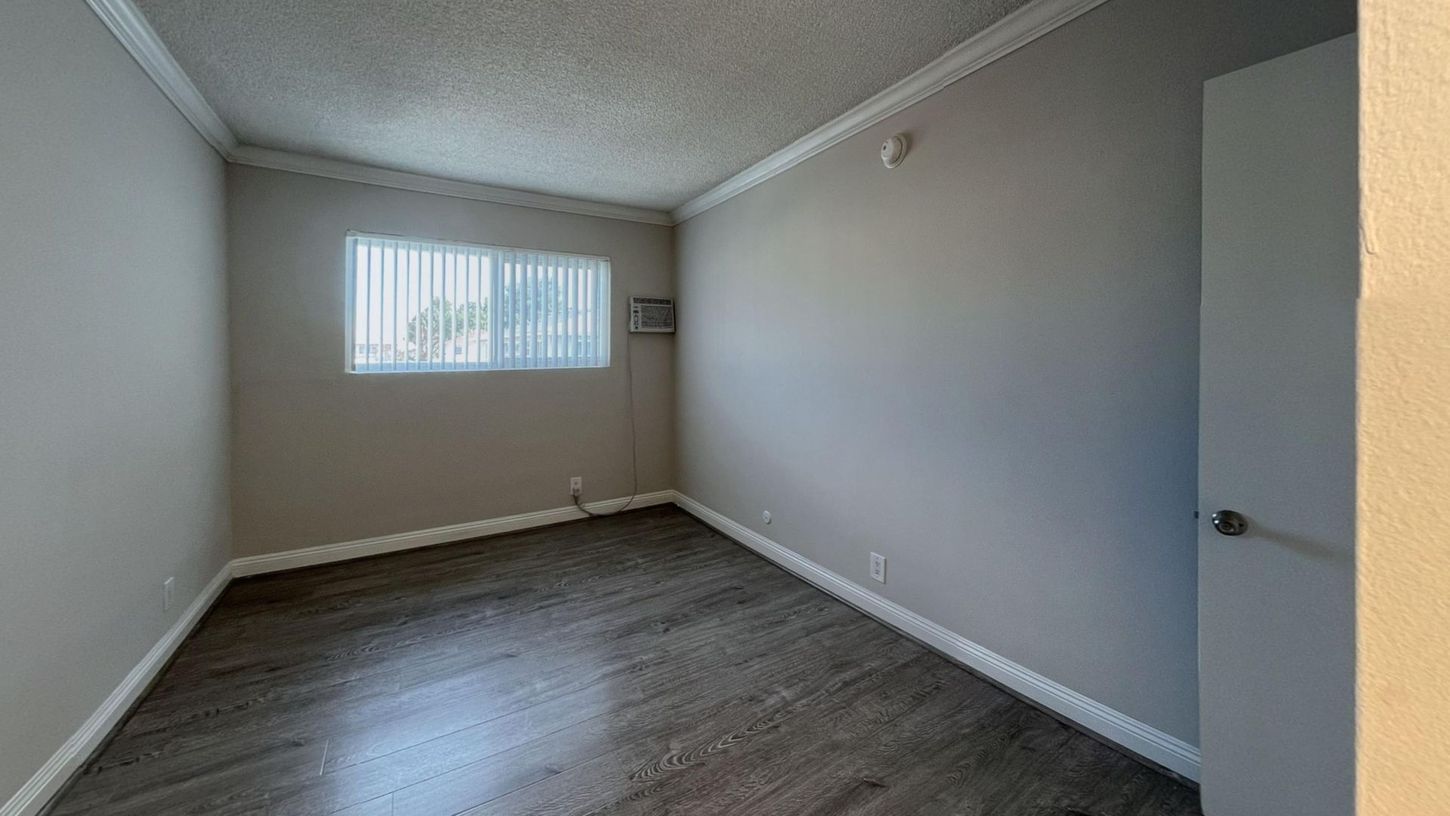 Empty room with gray walls, wood-look flooring, and a window with blinds.