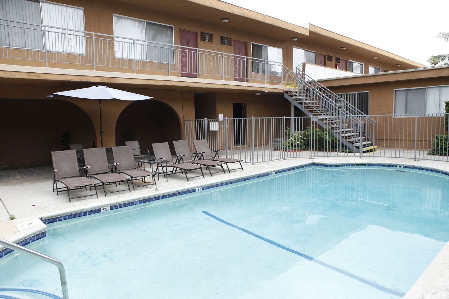 Swimming pool in front of a two-story apartment building with lounge chairs and a patio umbrella.